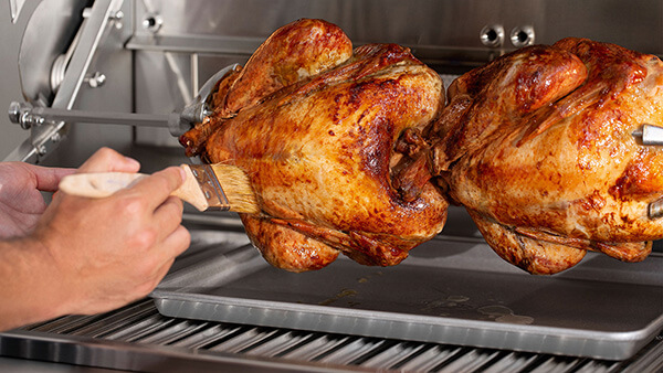 Close up of roasted whole chickens being glazed on rotisserie grill